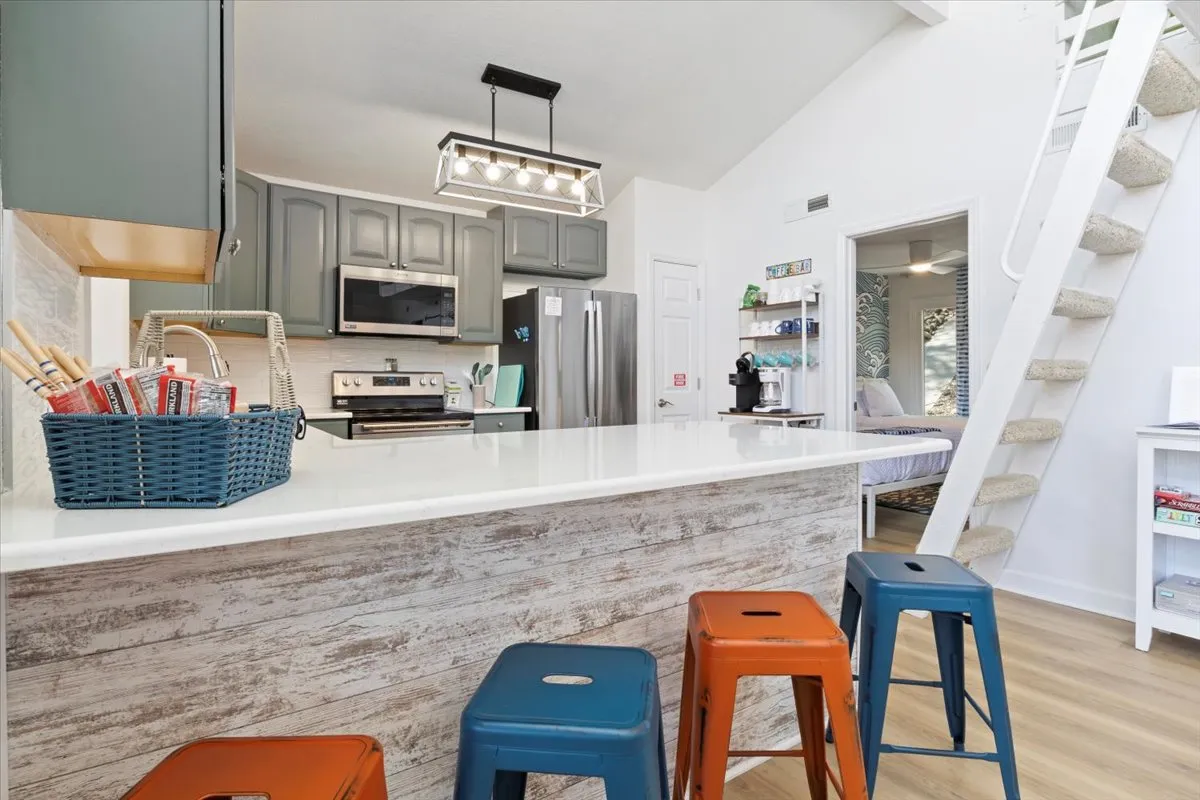 A modern, cheerful kitchen with a prominent island, colorful stools for casual seating, and sleek appliances. Open shelving provides both style and function, while the layout encourages both cooking and socializing—ideal for prepping snacks, hosting brunches, or sharing recipes.