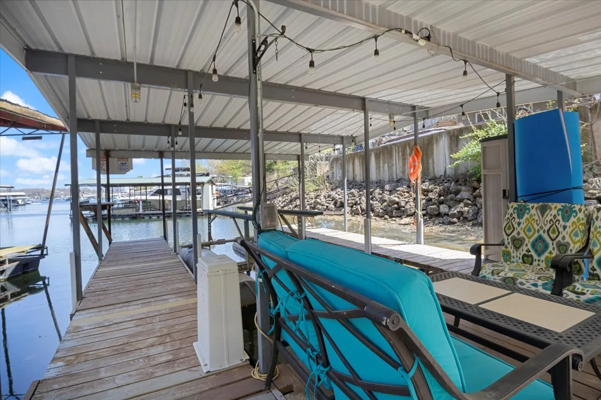 An exterior shot of a private dock with comfortable seating, decorative string lights, and a tranquil water view. The mood is leisurely, with the dock set up for relaxation, socializing, or launching water activities like boating or fishing. The setting is ideal for unwinding after work or enjoying sunset views over the lake.