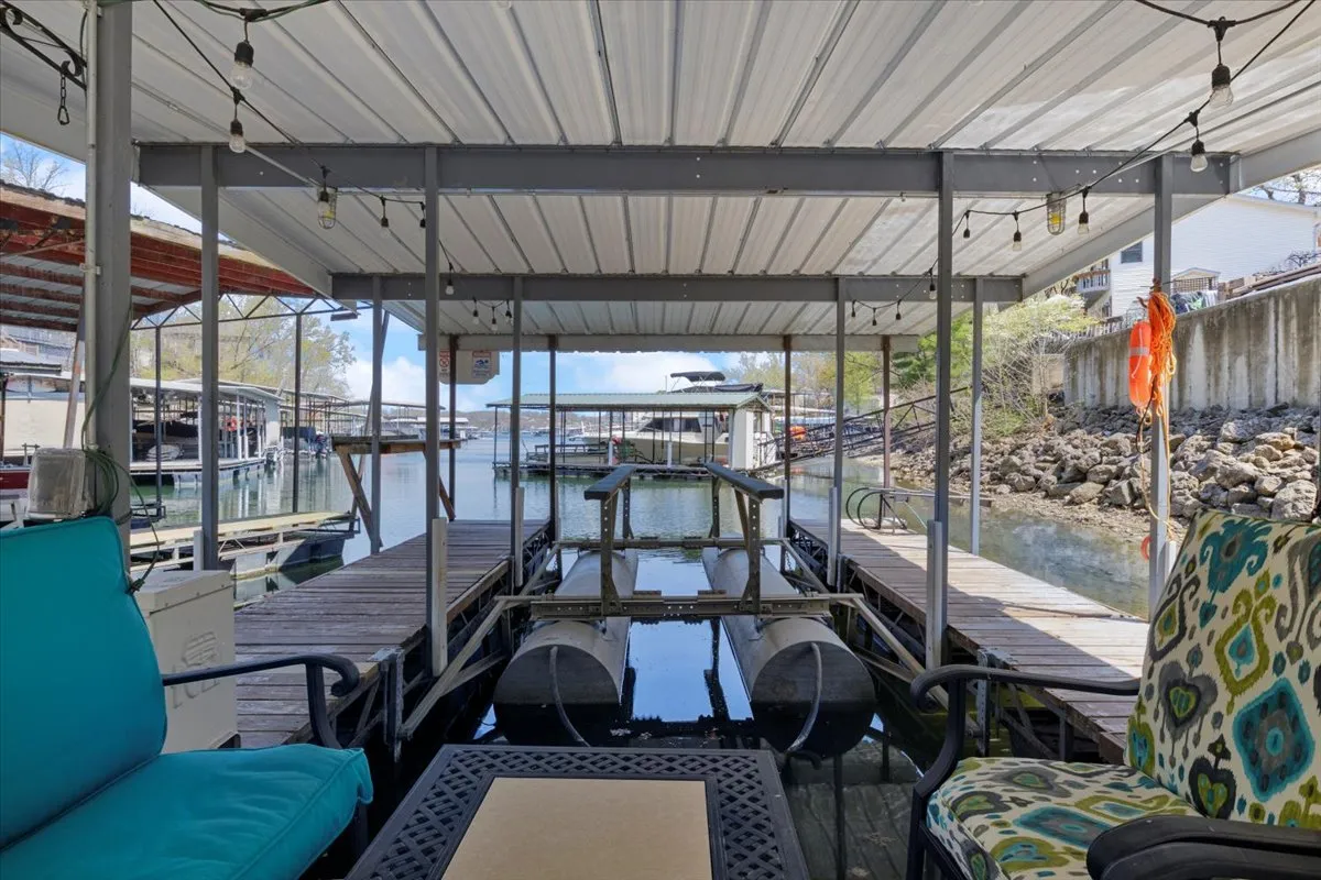 A tranquil lakeside dock stretches out over the water, with comfortable seating areas inviting guests to relax. The dock is bordered by scenic views of the lake and gentle hills, creating an idyllic spot for fishing, swimming, or simply enjoying time together. Boats are visible in the background, underscoring the range of lakeside activities available.