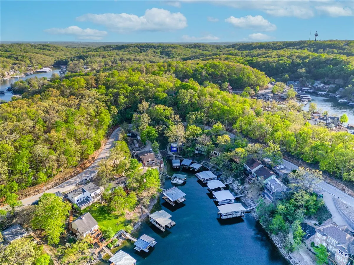 A picturesque view of lush green trees, calm water, boathouses, and a winding road creates a tranquil lakeside scene. The vantage point evokes the broader setting of the property, emphasizing connection to nature and opportunities for outdoor activities.