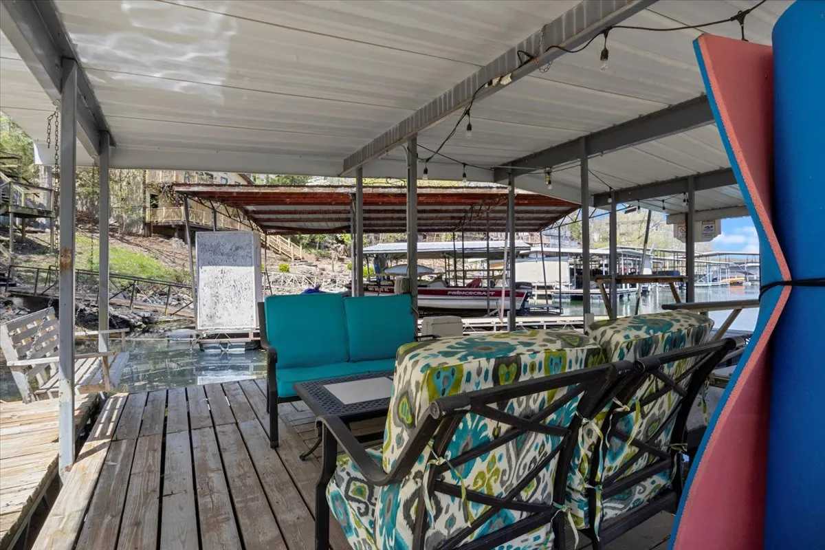 A lively wooden deck set with colorful seating offers direct access to the lake, alongside boat slips and a shaded canopy area. The inviting arrangement encourages group gatherings, leisurely mornings, and active afternoons on the water.