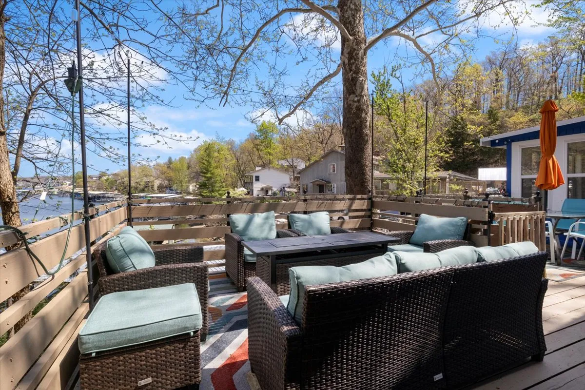 This exterior image features a welcoming outdoor seating area with a coffee table nestled beneath a leafy tree, providing both shade and serenity. The setup overlooks open space, hinting at a lakeside or natural environment perfect for relaxation and unwinding with a view.