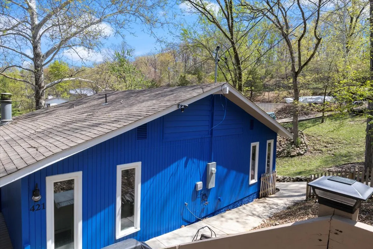 This image showcases the cheerful blue exterior of the house with large windows and abundant surrounding greenery. The inviting façade is set up for outdoor gatherings and relaxation, capturing the energetic yet peaceful spirit of the property.