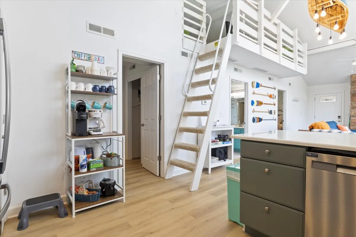 A view of a modern interior space with a staircase, inviting coffee bar, and kitchen island. The area feels designed for comfort and easy socializing, emphasizing thoughtful layouts and amenities.